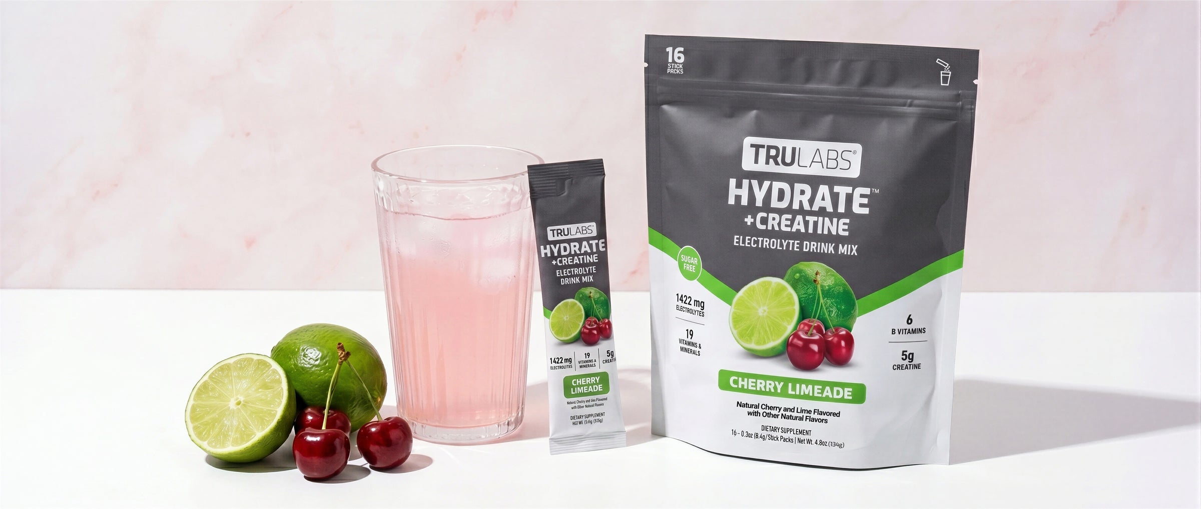 TruLass Hydrate + Creatine supplement package with a glass of pink drink and lime cherries on a light background